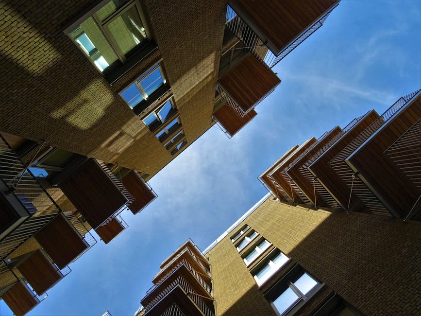 A multi-storey residential building with several balconies, some decorated with red and white flower boxes. A person is visible on one of the balconies, engaging with items or preparing for a home rel